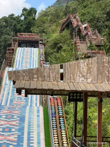 A slide with colorful patterned lanes running down a mountain slope, beside a staircase decorated with flowers