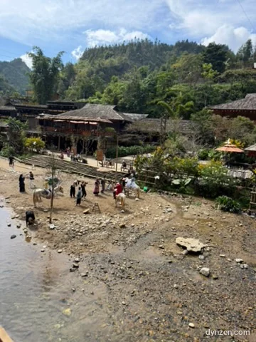 A gravel bank beside the stream, people in traditional costumes taking photos next to a model horse