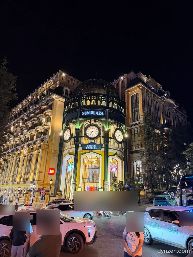 Sun Plaza at night, the green dome with three clocks and the ‘SUN PLAZA’ and ‘SAPA STATION’ signs lit up between yellow buildings