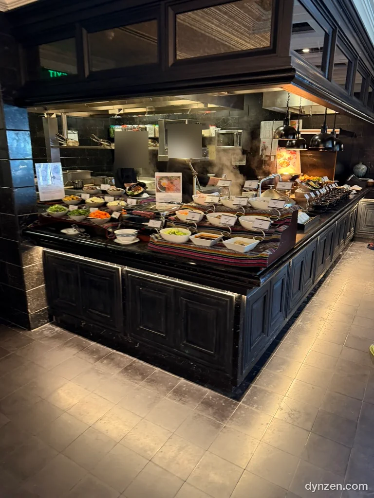 The Chic buffet, rows of side dishes on a black wooden counter and a steaming kitchen