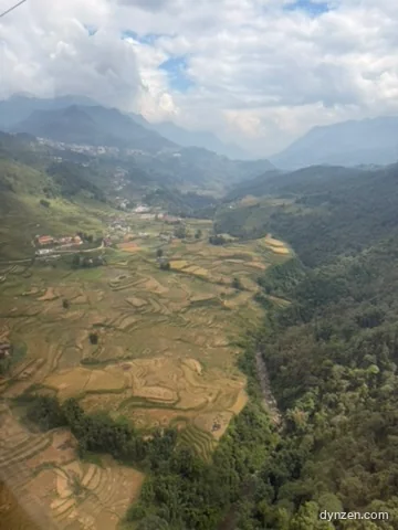 Out the descending cable car window, terraced rice fields and a deep valley in sunlight, with Sapa town in the distance