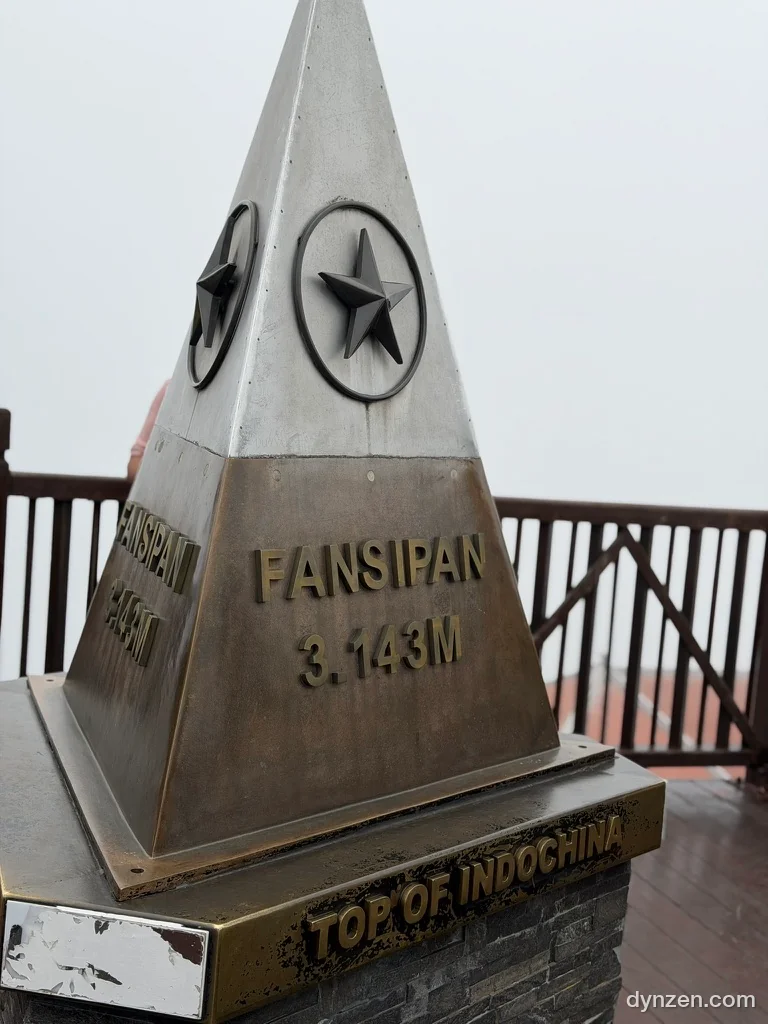 A triangular summit marker engraved ‘FANSIPAN 3.143M’ and ‘TOP OF INDOCHINA’, with white fog behind it