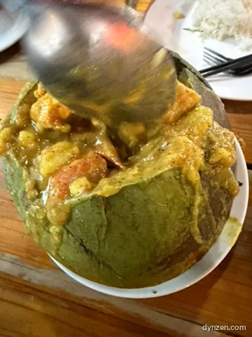 Yellow chicken curry in a halved coconut shell, being scooped with a spoon