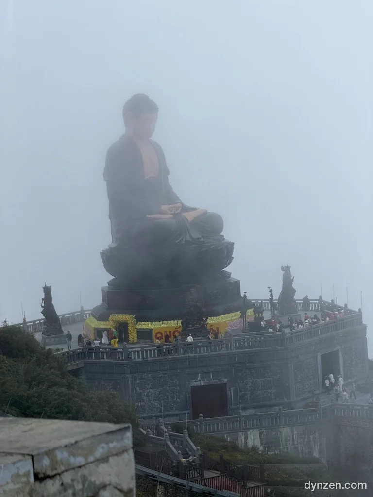 A huge Buddha statue sitting in fog on a stone base