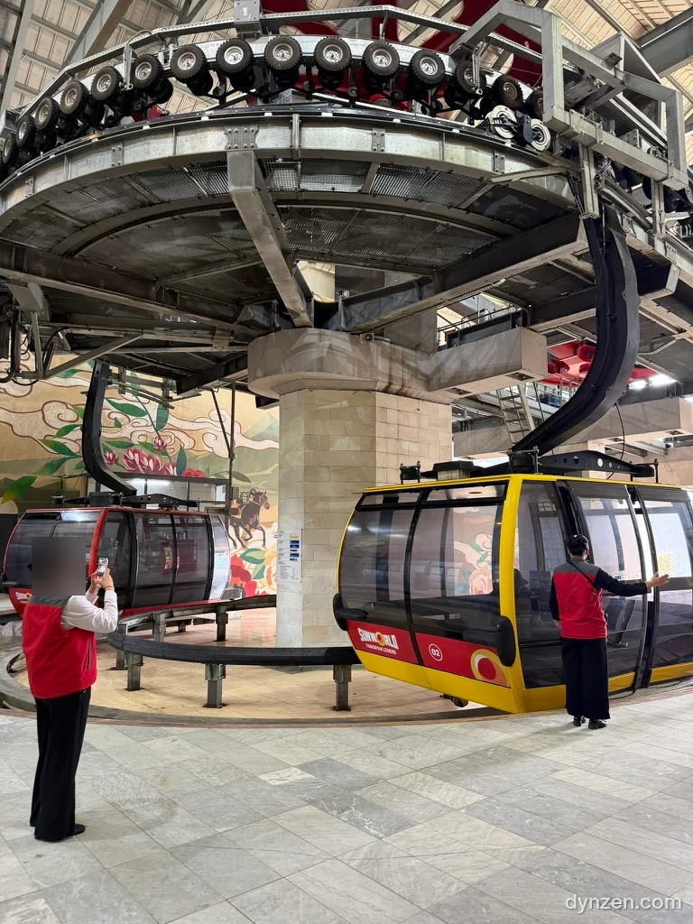 The Hoang Lien Station cable car platform, yellow cabins arriving under a large turning mechanism, staff in red vests