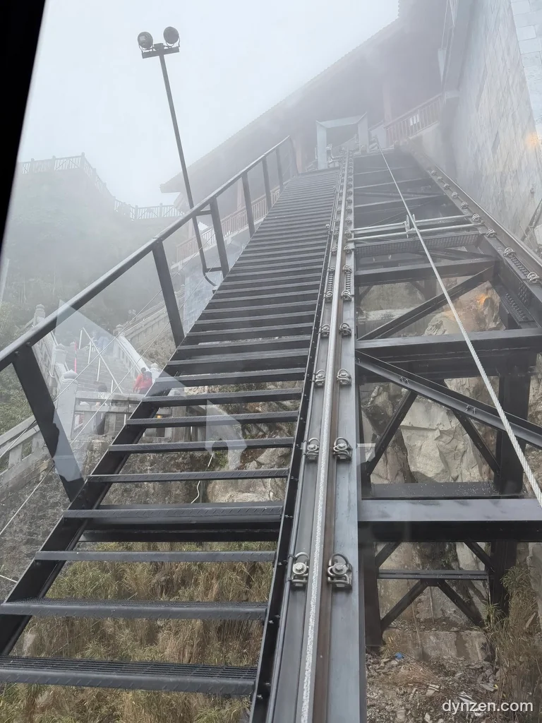 The steep rails of the summit train along a foggy mountain slope, with a metal staircase beside them