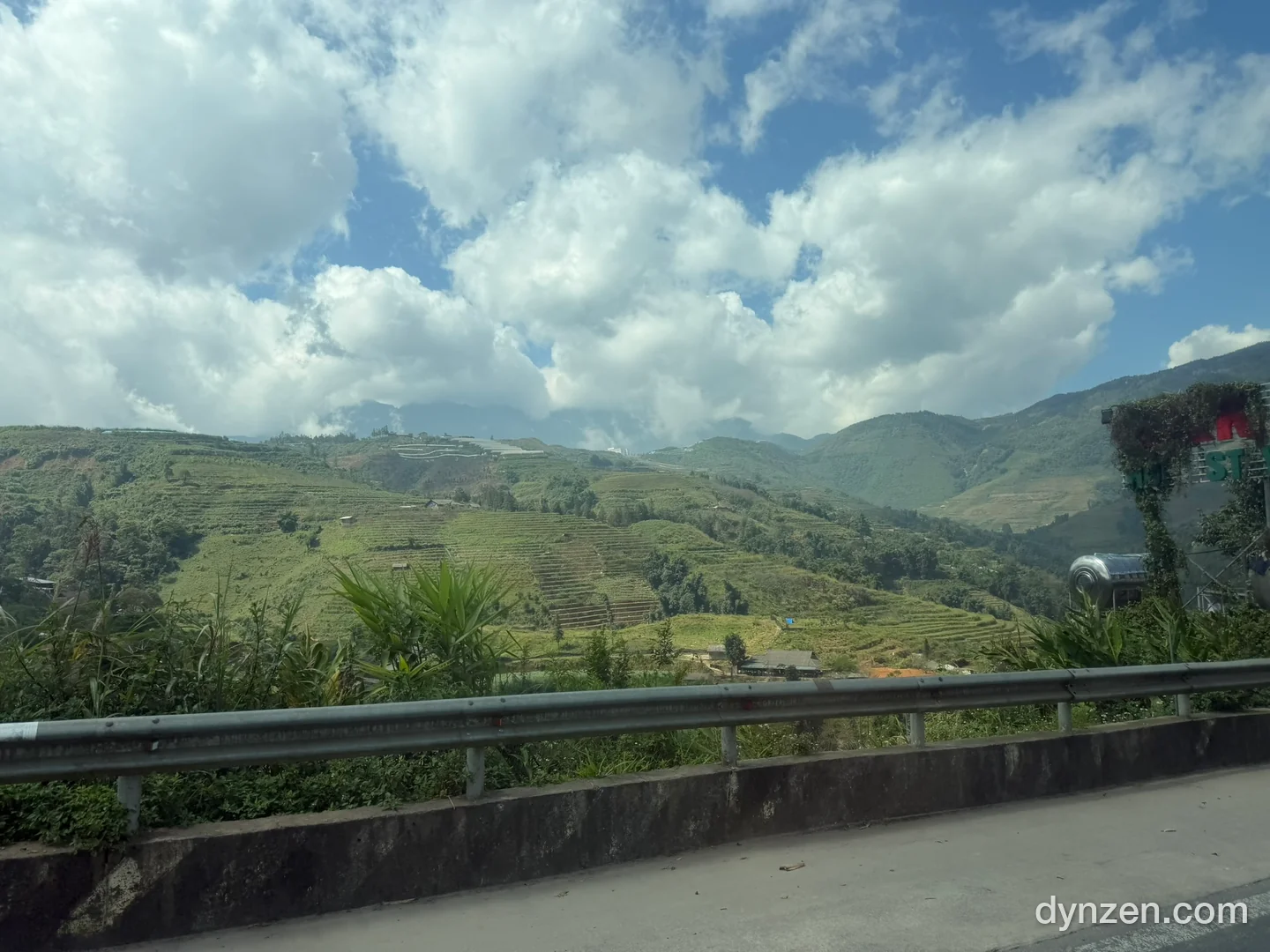 Terraced rice fields on a Sapa hillside and white clouds seen from the bus window, a guardrail in the foreground