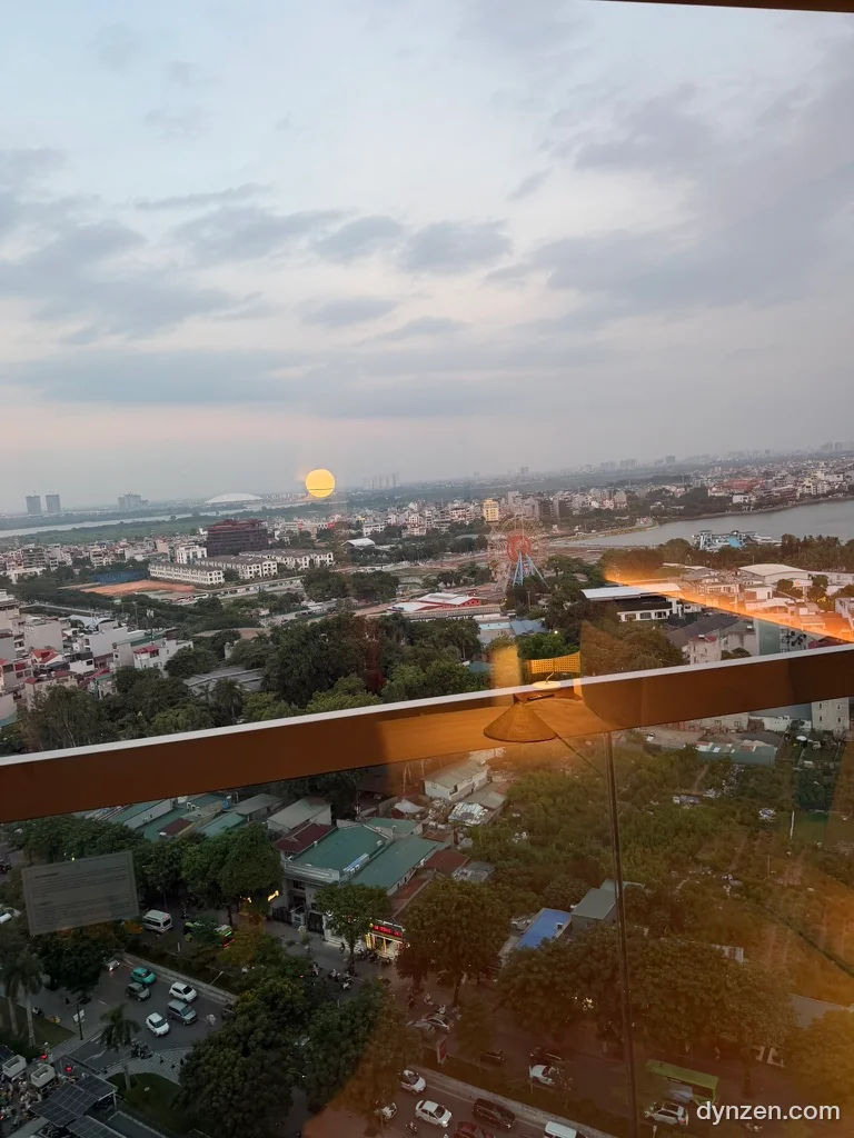 The view over Hanoi toward West Lake from the hotel room window, an orange sun resting on the horizon
