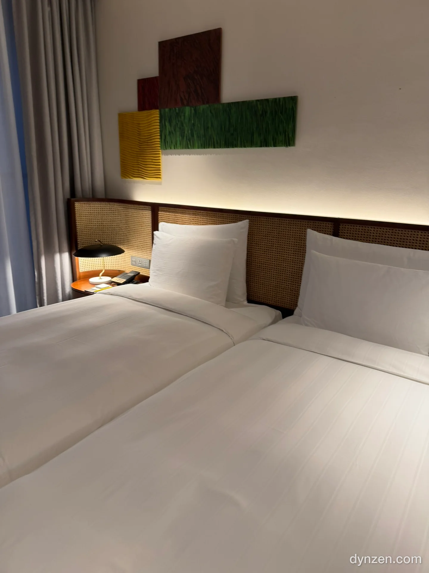 The L7 West Lake room, two single beds with white bedding and rattan headboards, green and yellow textile art on the wall