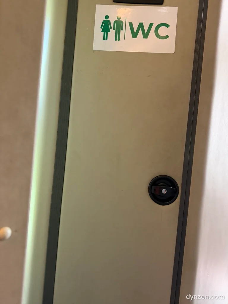 The toilet door inside the sleeper bus, a narrow sliding door with male and female symbols and a ‘WC’ sign
