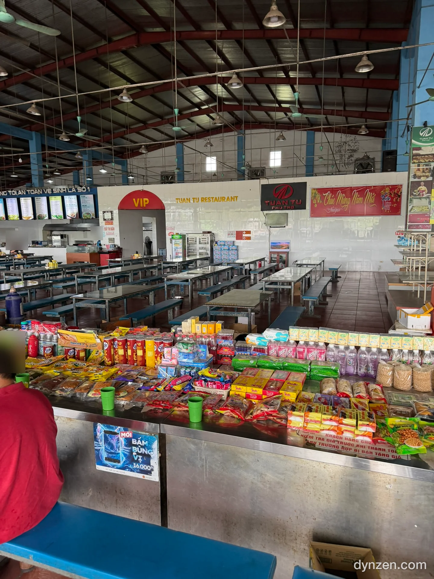 The large dining hall at the second rest stop, long tables and chairs behind a counter piled with snacks and drinks