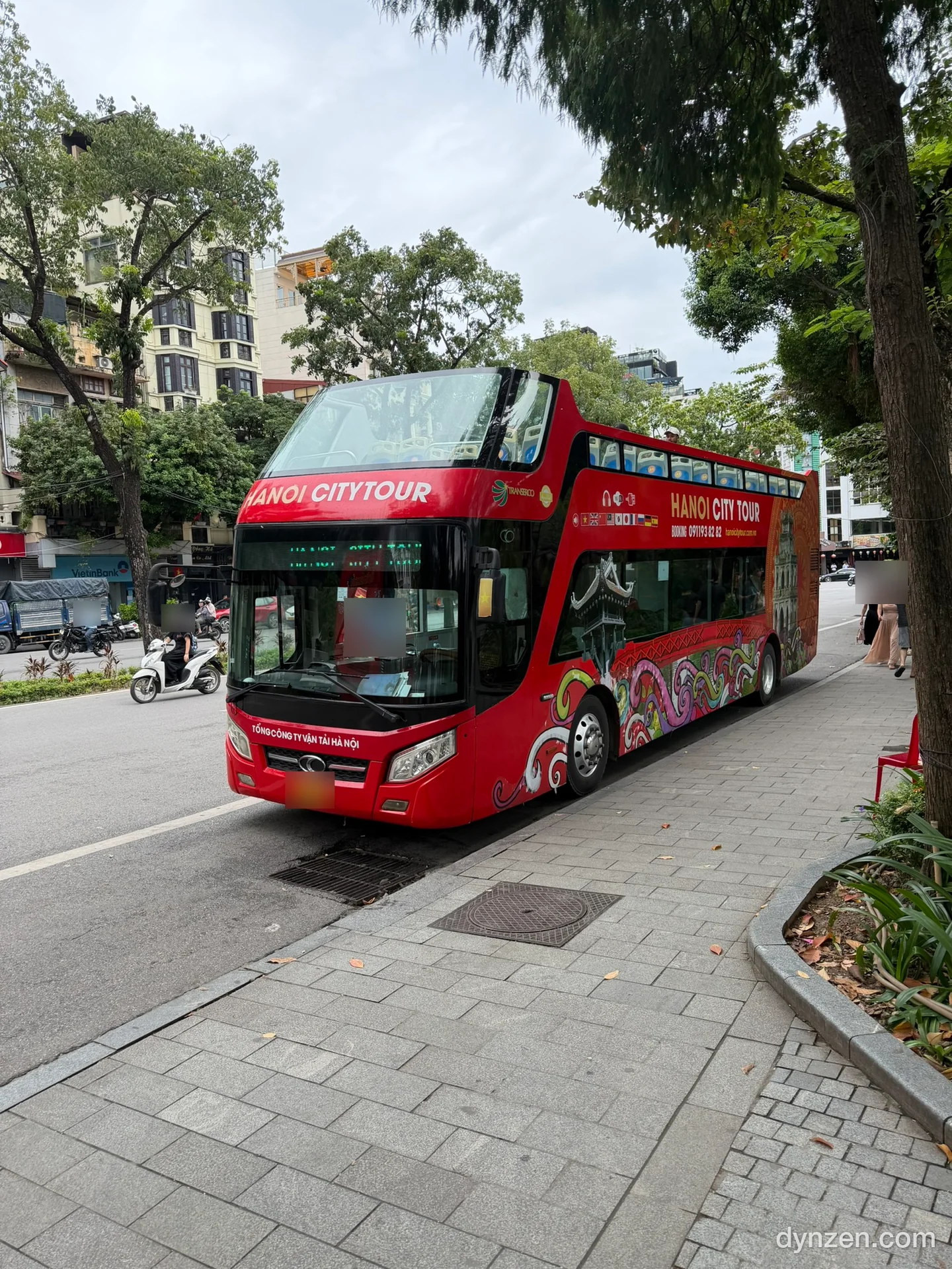 The red HANOI CITY TOUR double-decker bus parked on a Hoan Kiem street, open-top upper deck and a dragon painted on its side