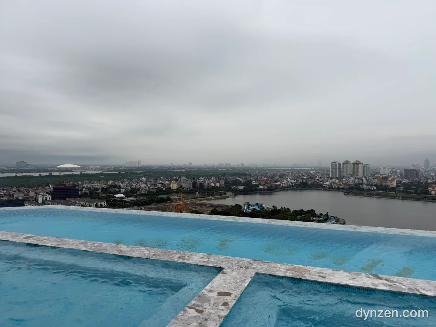 The L7 rooftop infinity pool, with West Lake and the Hanoi skyline under a hazy sky beyond the edge of the water