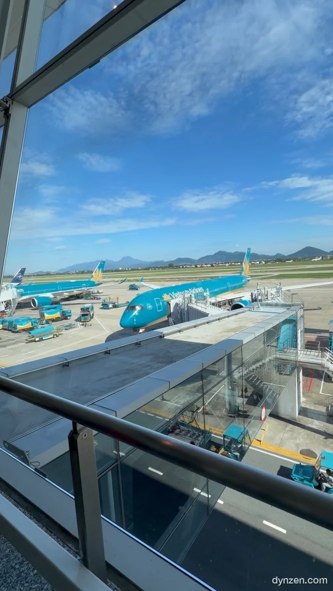 Several Vietnam Airlines planes at the jet bridges of Noi Bai International Airport, mountains in the distance under a clear sky